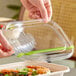 A clear compostable plastic lid being placed on a fiber food container.