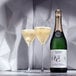 A bottle of Noughty Non-Alcoholic Sparkling Chardonnay and two glasses of yellow liquid on a table.