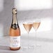 A bottle of Noughty Non-Alcoholic Sparkling Rose next to two glasses of champagne.