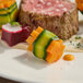 A mini carrot bundle wrapped with a strip of zucchini, served as part of a plated dish.