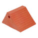 A large orange plastic dual slope wheel chock with a ridged surface and a hole on one side.