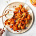 A plate with roasted cauliflower and a spoon with food on it next to a bowl of white sauce.