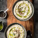 Two bowls of creamy cauliflower soup with green and brown toppings.