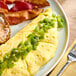 An omelet topped with diced green peppers served on a plate with bacon and a slice of bread.