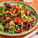 A plate of mixed greens salad topped with diced red peppers, crumbled cheese, and pine nuts.
