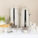 Two Bon Chef Roman stainless steel coffee chafer urns on a table with plates and cups.