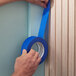 A roll of blue painter's masking tape being applied to a wall edge.