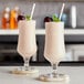 Two glasses of frozen frose with cherries on a bar.