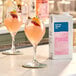 A 32 fl. oz. carton of Kelvin Slush Co. Organic Frozen Frosé Cocktail Mix displayed next to two glasses of pink frozen cocktail garnished with fruit and a decorative pick.