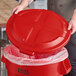 A red round dome trash can lid being placed on a matching Lavex 32-gallon trash can.