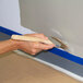A roll of blue painter's masking tape being used to create clean paint lines on a wall.