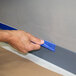 A hand applying blue painter's masking tape along the edge of a wall and baseboard.