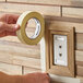 A roll of general purpose masking tape being applied to a wall near a wooden-framed outlet.