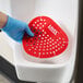 A red vinyl deodorizing urinal screen being placed in a urinal.