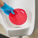 A red vinyl deodorizing urinal screen being placed in a urinal.