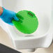A green vinyl deodorizing urinal screen being placed in a urinal.