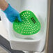 A green vinyl deodorizing urinal screen being placed in a urinal.