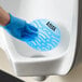 A blue Lavex deodorizing gel urinal screen being placed in a white urinal by a person wearing a blue glove.