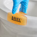 A Lavex mango scent toilet bowl clip being placed on the rim of a toilet by a person wearing a blue glove.