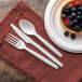 A white napkin with a spoon, fork, and knife on a plate of fruit.
