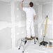 A portable aluminum work platform being used by a person for painting or construction tasks.