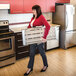 A woman carrying a folded Metaltech Jobsite 30-inch aluminum portable work platform in a kitchen.