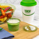A green Eco-Products compostable plastic lid on a cup of green liquid with a white and green bowl of vegetables.