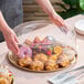 A clear round high dome plastic catering tray lid being placed over a tray of assorted pastries.