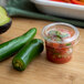 A plastic container of salsa and jalapenos on a counter.