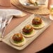 A rectangular sand dollar porcelain plate with food and a glass of water on a table.