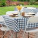 A navy and white gingham vinyl table cover with a flannel back, shown on a square table set for an outdoor meal.