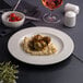 A white round porcelain plate with an embossed wide rim, shown with food served on it.
