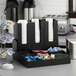 A black bamboo coffee condiment organizer with nine compartments and removable cup holders, holding cups, creamers, sweeteners, and tea bags.