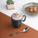 A charcoal grey porcelain cup filled with coffee and whipped cream with a spoon on the saucer.