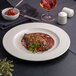 A white round embossed wide rim flat porcelain plate with food artfully presented on it.
