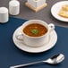 A white round embossed wide rim soup bowl saucer with a soup bowl placed on top.
