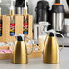 A gold stainless steel coffee carafe with a handle and spout, designed for serving hot beverages.
