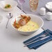 A large warm white porcelain nappie bowl filled with a creamy seafood dish, shown on a set dining table.