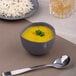 An Ariane charcoal grey porcelain bowl filled with soup on a table.