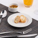 A round, warm white porcelain plate with a wide rim, shown with two pieces of bread on it.