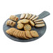 A round gray faux wood melamine serving board with a handle, displayed with assorted cookies and pastries.
