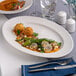 A warm white oval wide rim porcelain platter with food served on it.