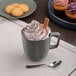 An Ariane mist green porcelain mug filled with hot chocolate topped with whipped cream and cinnamon.