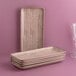 A stack of Ariane rectangular porcelain plates on a pink surface.