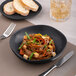 A Charcoal Grey Dots porcelain plate with noodles, vegetables, and tofu on it.