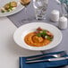 A round, wide rim deep white porcelain plate with food served on it.
