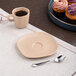A plate with an Ariane Dark Sand Dots porcelain saucer and a cup of coffee with a spoon and cupcakes on a table.