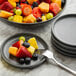 A stack of small, round, speckled gray melamine plates with one plate holding assorted fruit and a fork.