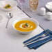 A warm white porcelain nappie bowl filled with soup, placed on a table setting with cutlery and a napkin.
