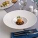 A white round wide rim deep porcelain gourmet plate with a small food portion in the center.